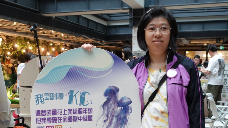 老闆KC手持印有自己畫畫創作的簡介牌子，上面印有由自己畫的水母畫作，展現滿足開心樣子。