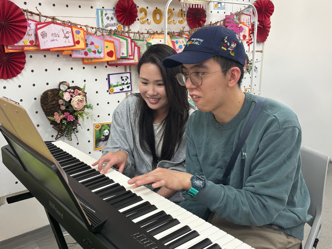 鋼琴老師劉老師臉帶笑容指導阿邦學習彈奏新曲，阿邦認真學習，十分投入。