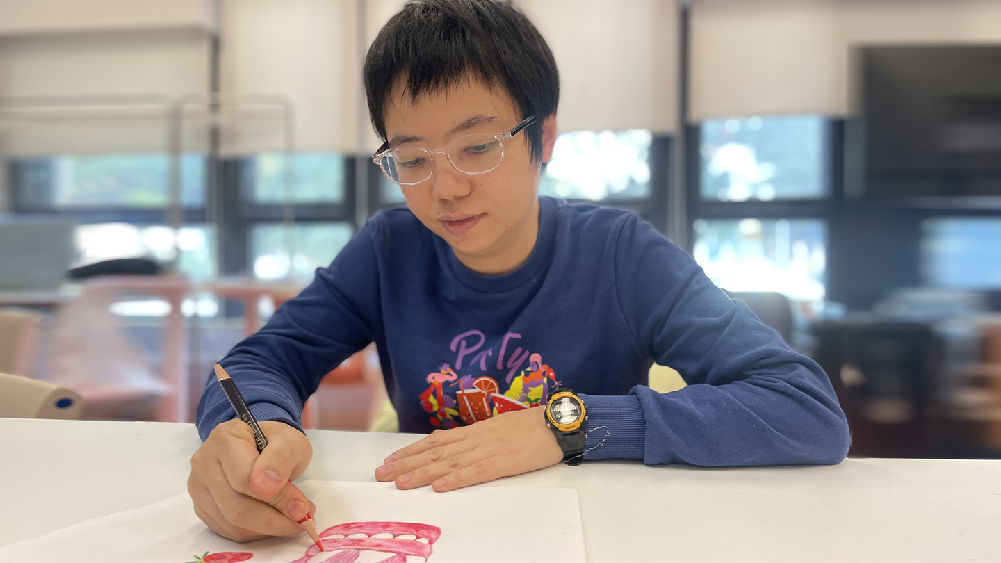 老闆Mini正在畫紙上畫畫，專注於他的創作過程。